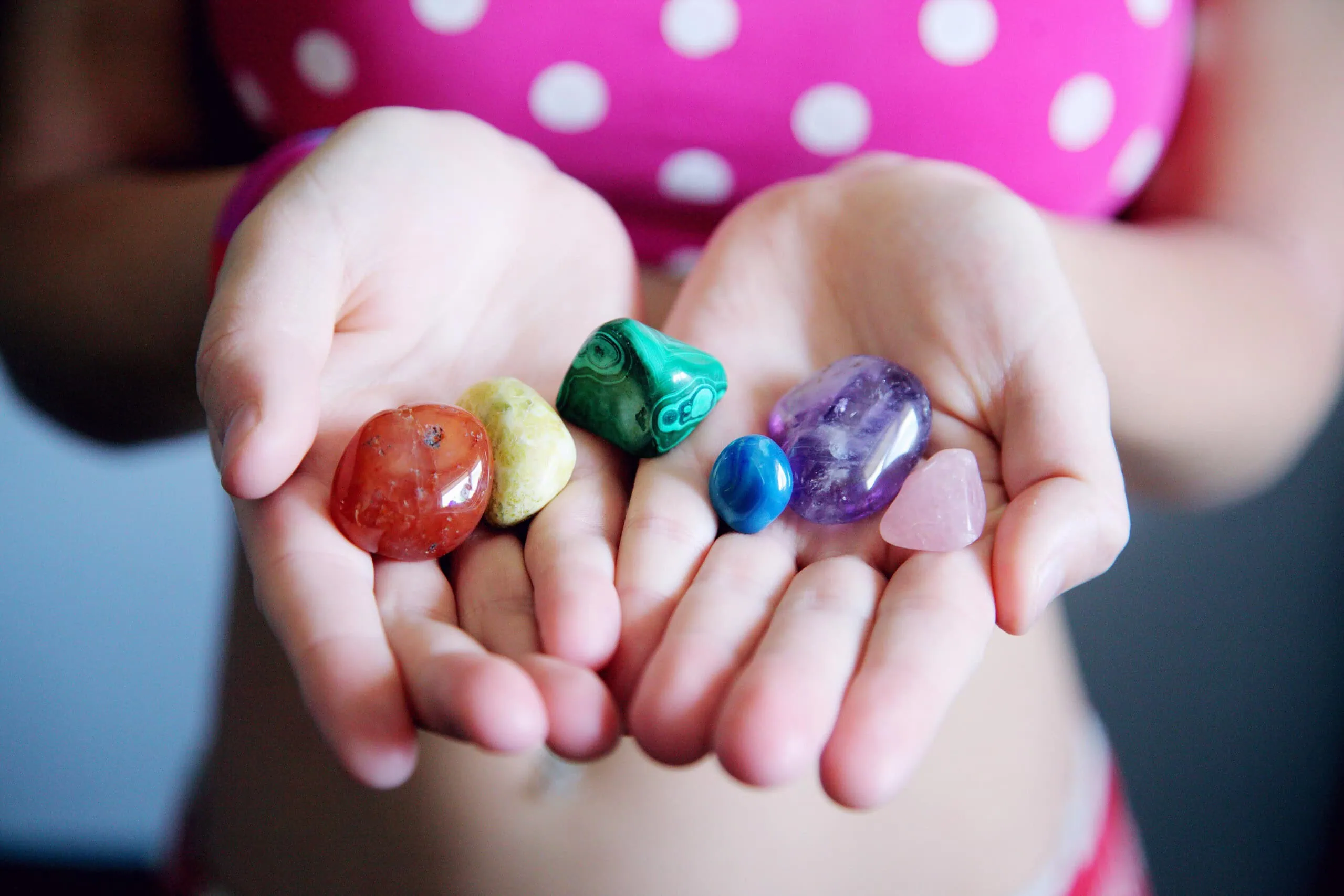 Ein Kind hält eine Sammlung bunter, bearbeiteter Edelsteine in seinen offenen Handflächen.