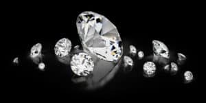 Verschiedene geschliffene Diamanten auf einer reflektierenden Oberfläche mit schwarzem Hintergrund, erkennbar als „Diamanten als Heilsteine“.