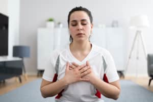 Frau praktiziert während einer Reiki-Behandlung tiefe Atemübungen mit geschlossenen Augen und den Händen auf der Brust.