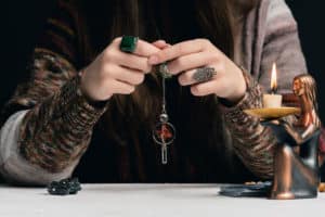 Eine Person führt eine Wünschelrutensitzung mit Heilsteinen durch, in deren Nähe sich eine Kerze und eine Figur befinden.