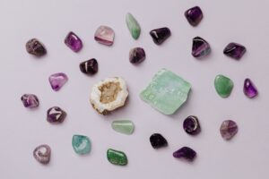 Verschiedene Halbedelsteine und Kristalle in unterschiedlichen Formen und Farben, angeordnet auf einem hellrosa Hintergrund.