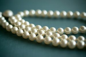 Eine Schnur berühmter weißer Perlen, auf einer blauen Stoffoberfläche ausgelegt.
