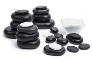 Schwarze und weiße glatte Steine, bekannt als Handschmeichler, in Stapeln mit einem quadratischen Behälter aus klarem Glas auf weißem Hintergrund.