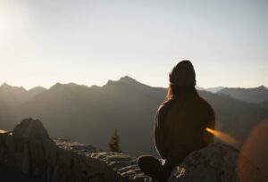 Eine Person, die bei Sonnenuntergang auf einem Felsen sitzt und auf eine Berglandschaft blickt, verkörpert die besten Tipps zum Trainieren ihres Unterbewusstseins.