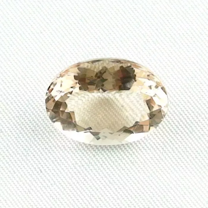 Ein facettierter, ovaler Edelstein mit einem hellbraunen Farbton ist auf einer strukturierten weißen Oberfläche platziert.