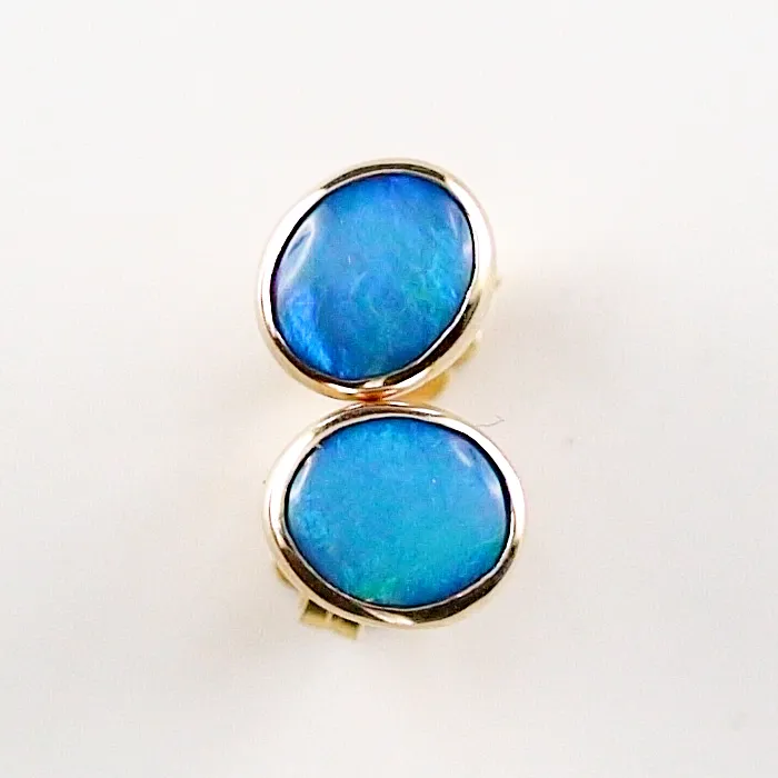 Ein Paar ovale Ohrringe aus blauem Opal mit goldfarbenen Fassungen auf schlichtem weißen Hintergrund.