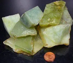 Zum Größenvergleich werden mehrere Stücke groben grünen Jades neben einem Penny ausgestellt.