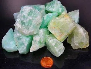 Zum Größenvergleich ist neben einem Penny ein Haufen grüner Kalzitkristalle abgebildet.