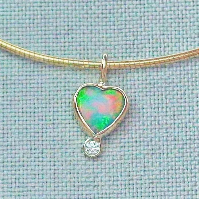 Eine goldene Halskette mit einem herzförmigen Opalanhänger und einem kleinen Diamanttropfen vor einem strukturierten Stoffhintergrund.