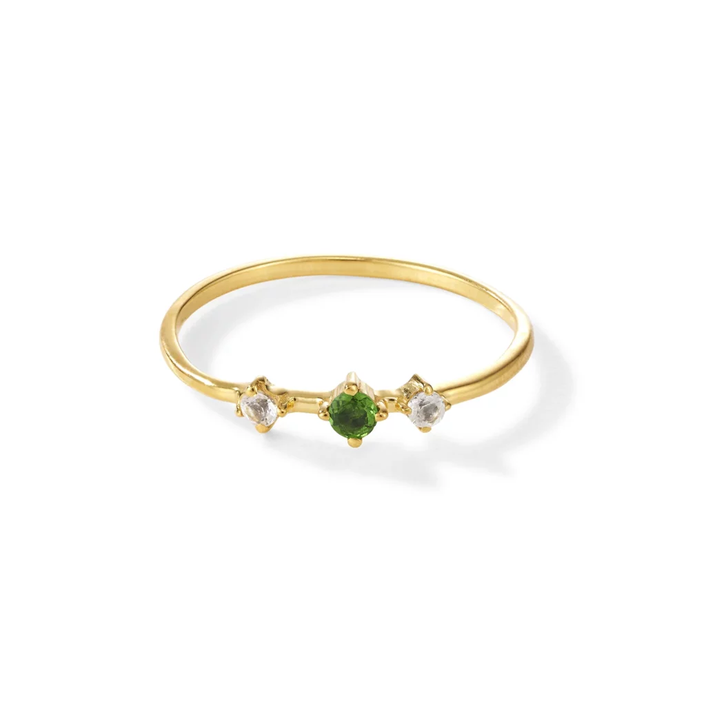 Ein Goldring mit einem grünen Edelstein in der Mitte, flankiert von zwei kleineren klaren Edelsteinen auf einem schlichten Goldband.