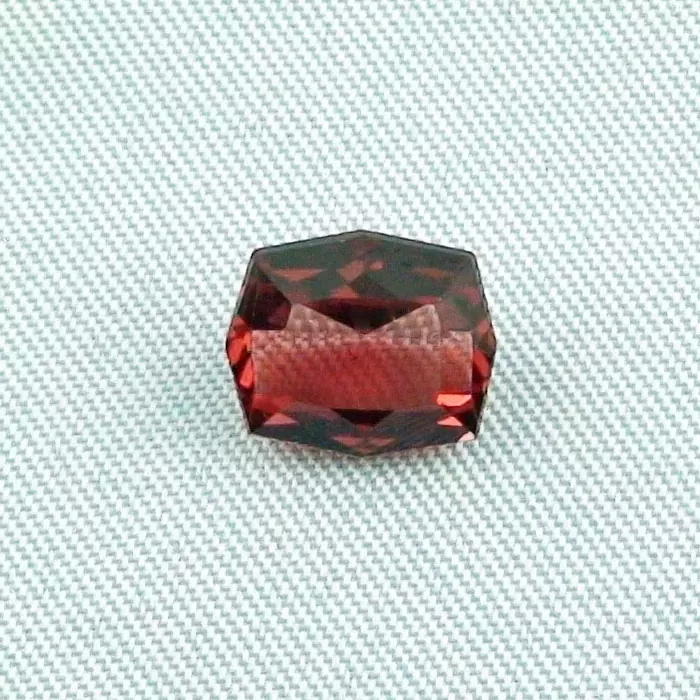 Ein sechseckiger, facettierter roter Edelstein wird auf einer strukturierten, hellen Oberfläche präsentiert.