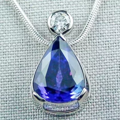 Ein tropfenförmiger Anhänger aus blauem Edelstein mit einem darüber angebrachten kleinen runden Diamanten, an einer silbernen Halskette, auf einem strukturierten grauen Hintergrund.