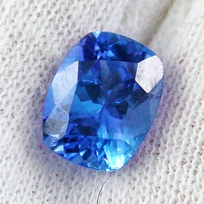 Eine Nahaufnahme eines blauen Saphir-Edelsteins, der auf einer strukturierten weißen Stoffoberfläche ruht.