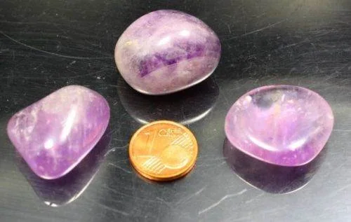 Drei polierte Amethyststeine auf einer dunklen Oberfläche mit einer 1-Cent-Münze als Maßstab.