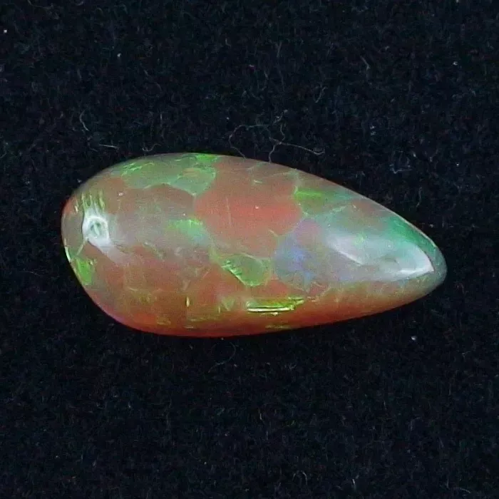 Ein birnenförmiger Opal-Edelstein in einer Reihe leuchtender Farben, darunter Grün, Rot und Orange, auf schwarzem Hintergrund.
