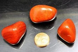 Drei polierte rote Steine sind um eine 1-Cent-Euromünze auf schwarzem Untergrund angeordnet.