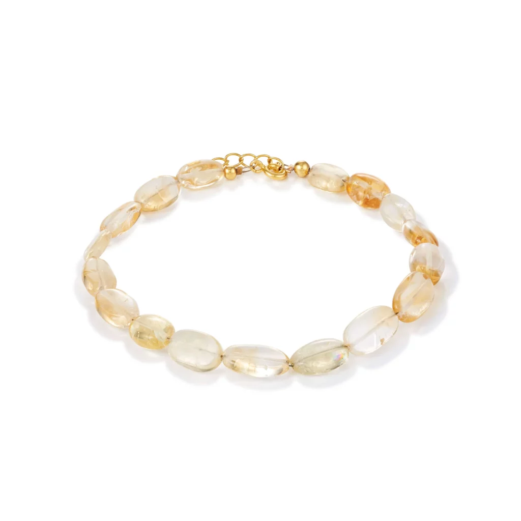 Ein Armband aus ovalen, halbtransparenten Perlen in einem hellen Bernsteinton, mit einem kleinen goldenen Verschluss und einer Kette zum Verstellen.