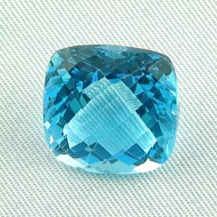 Ein facettierter blauer Edelstein in Kissenform ist auf einer hellgrauen, strukturierten Oberfläche platziert.