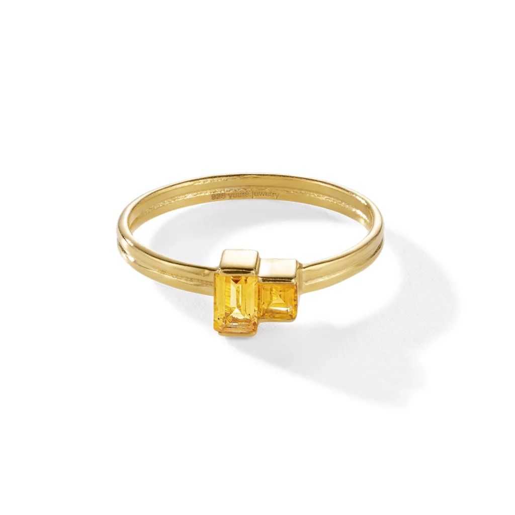 Ein goldener Ring mit zwei nebeneinander liegenden rechteckigen gelben Edelsteinen auf weißem Hintergrund.