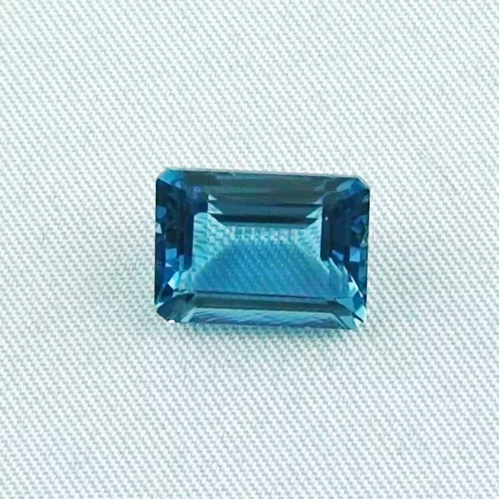 Ein rechteckiger blauer Edelstein mit abgeschrägten Kanten ist auf einer strukturierten, hellen Oberfläche platziert.