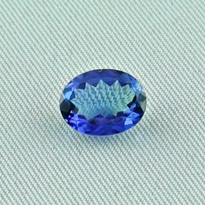 Ein facettierter ovaler blauer Edelstein auf einer hellgrauen strukturierten Oberfläche.