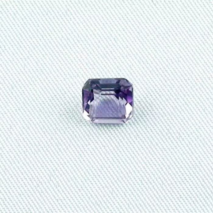 Ein rechteckig geschliffener violetter Edelstein ist auf einem hellgrauen, strukturierten Hintergrund platziert.