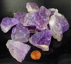 Zur Veranschaulichung werden mehrere Rohstücke violetter Amethyst-Edelsteine mit einem Penny angezeigt.