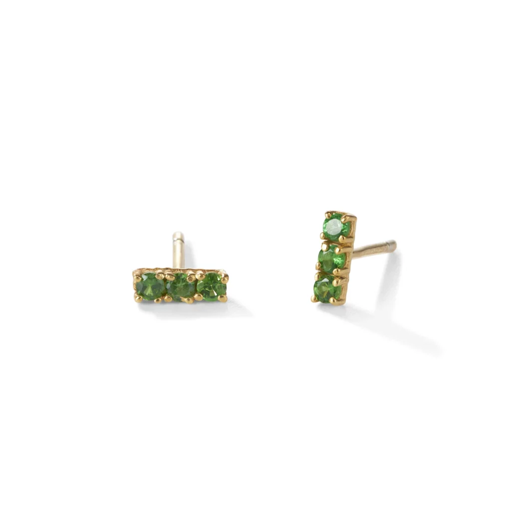 Paar goldene Ohrstecker mit drei kleinen grünen Edelsteinen in rechteckiger Anordnung, aus zwei Winkeln gezeigt.