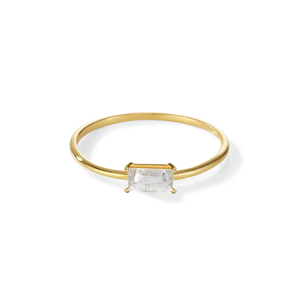 Ein goldener Ring mit einem rechteckigen, klaren Edelstein in einer einfachen Krappenfassung.