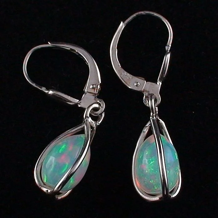 Ein Paar silberne Tropfenohrringe mit ovalen Opalsteinen und einem Hebelverschluss vor schwarzem Hintergrund.