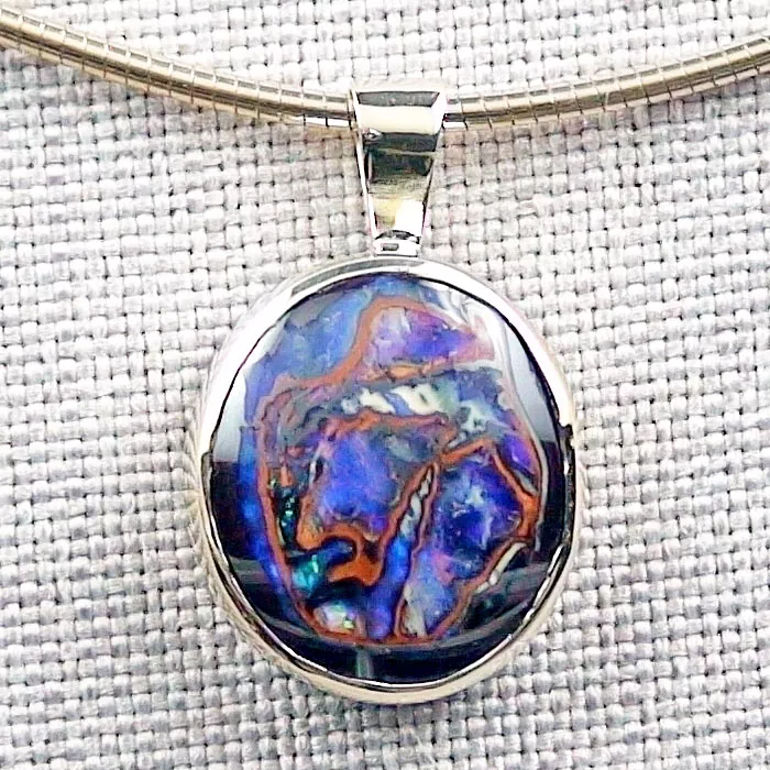 Eine silberne Halskette mit Anhänger, die einen ovalen Stein mit wirbelnden Mustern in Blau, Lila und Braun vor einem strukturierten beigen Hintergrund aufweist.