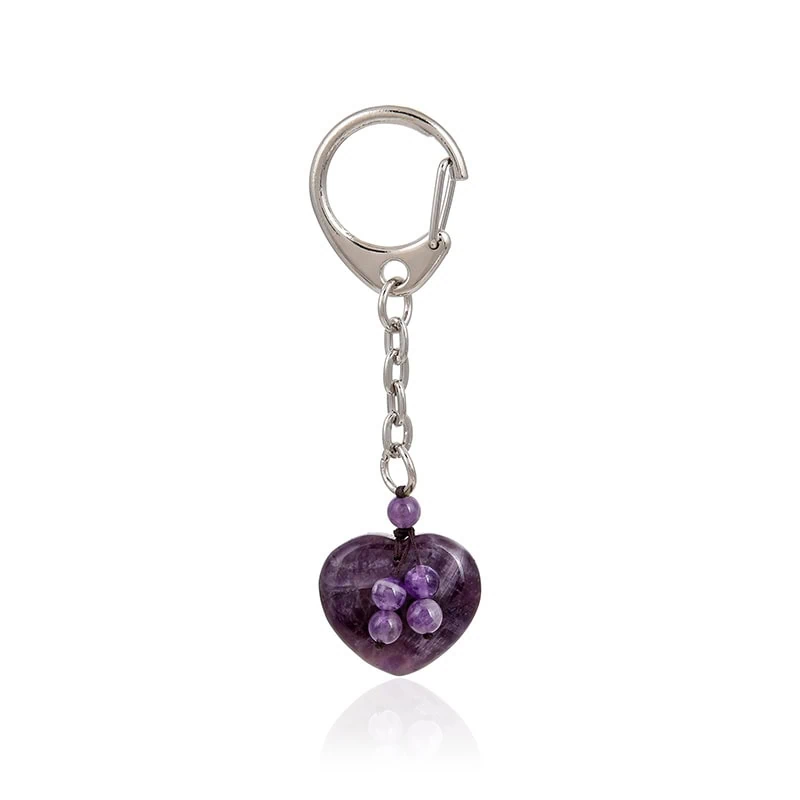 Ein silberner Schlüsselanhänger mit einer Metallkette verfügt über einen violetten herzförmigen Anhänger, der mit kleinen runden violetten Perlen in einem Blumenmuster verziert ist.